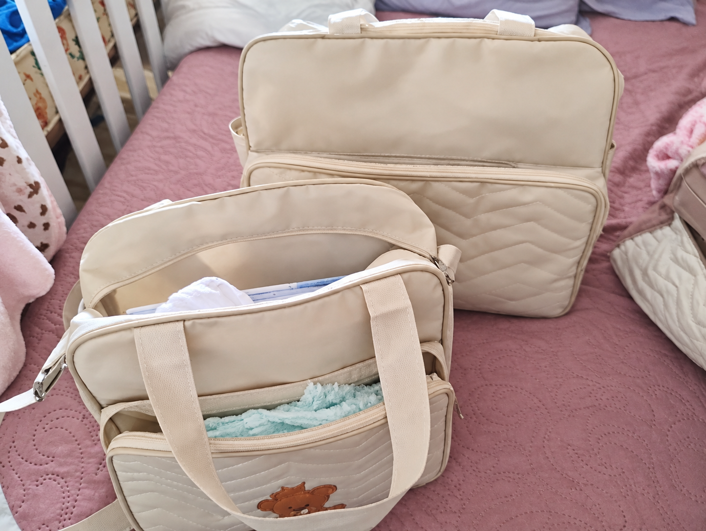 Duas bolsas maternidade bege sobre a cama, com a bolsa pequena aberta à frente.